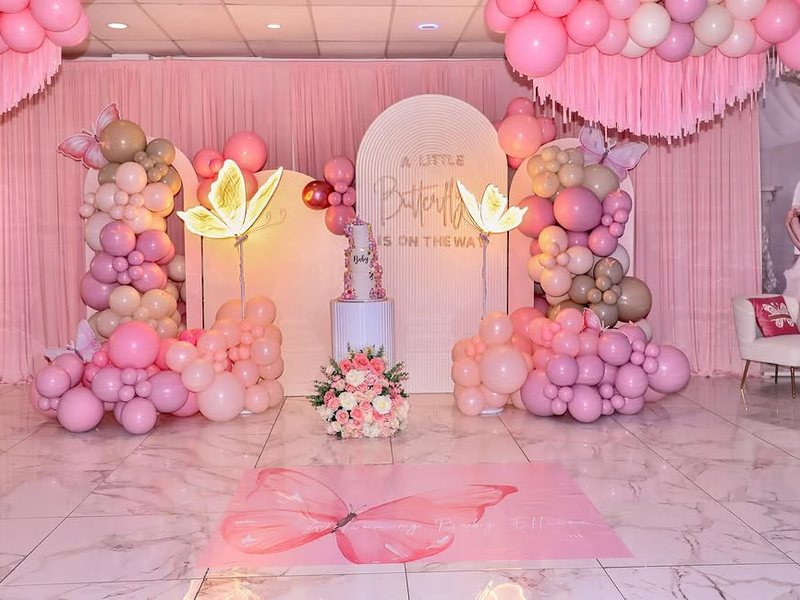 A pink butterfly baby shower with balloon garlands, arch walls and a butterfly floor vinyl